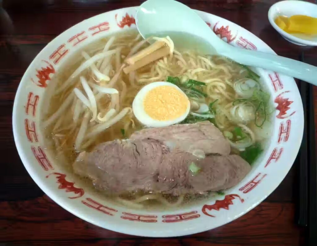 Tottori gyukotsu ramen in a white bowl with bean sprouts, menma, chashu, half a boiled egg and green onion in a pale golden broth
