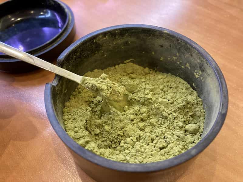 Bowl of konacha, the fine, sandy particles sifted from Japanese green tea leaves, with a metal spoon.